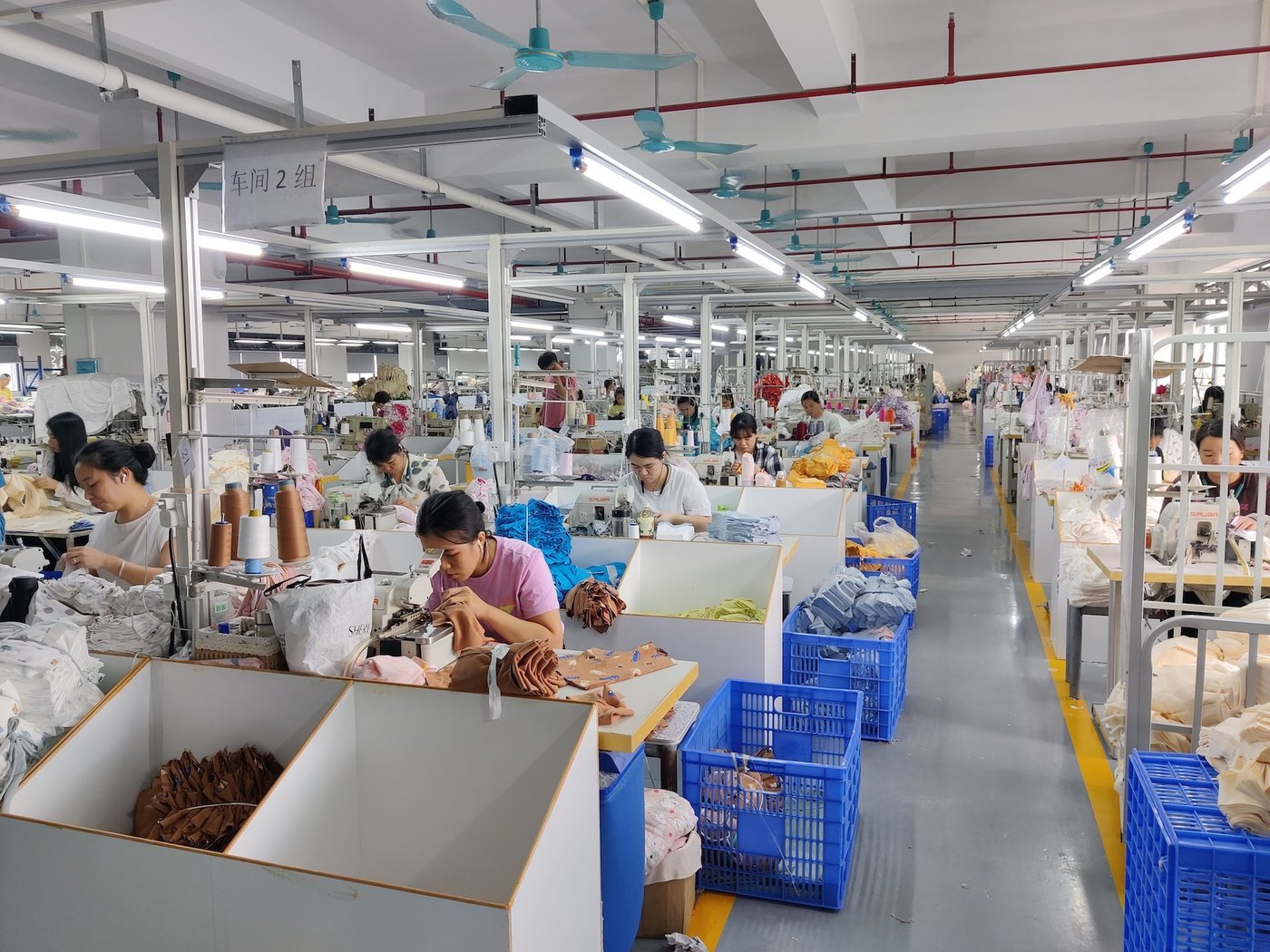 A garment sewing line with blue bins alongside the machines A garment sewing line with blue bins alongside the machines