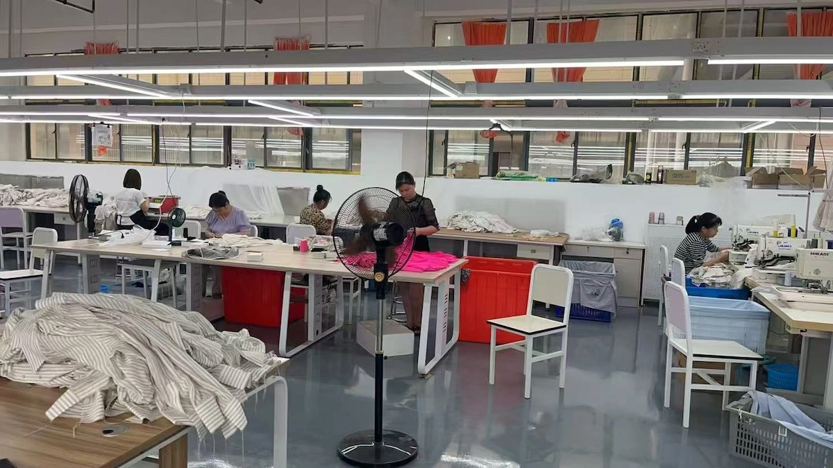 A sewing workshop with workers at machines and red bins along the line A sewing workshop with workers at machines and red bins along the line