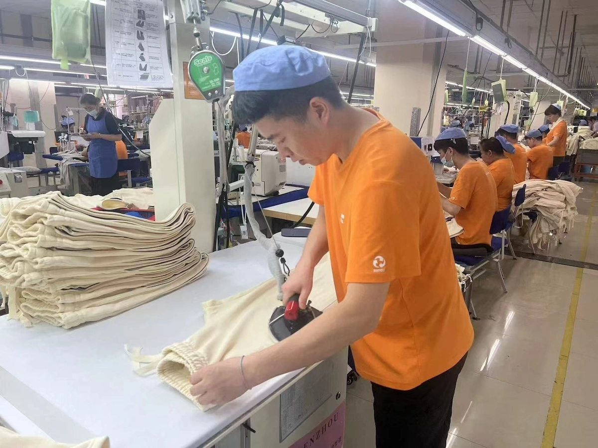 A worker pressing cream garments on a production line A worker pressing cream garments on a production line