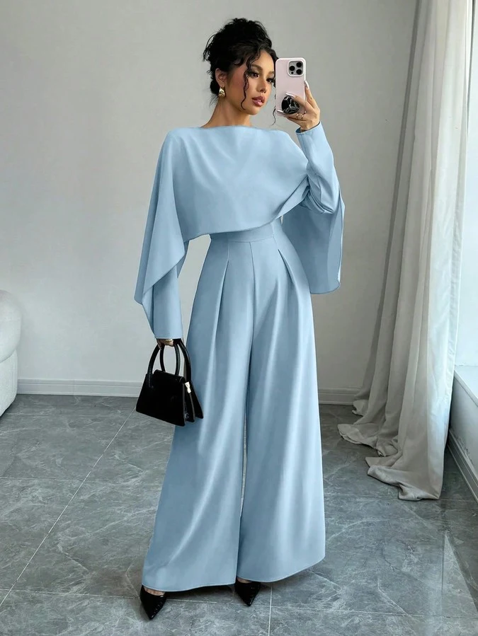 Front view of the light blue cape-overlay tie-waist wide-leg jumpsuit, showing the silhouette and fit.