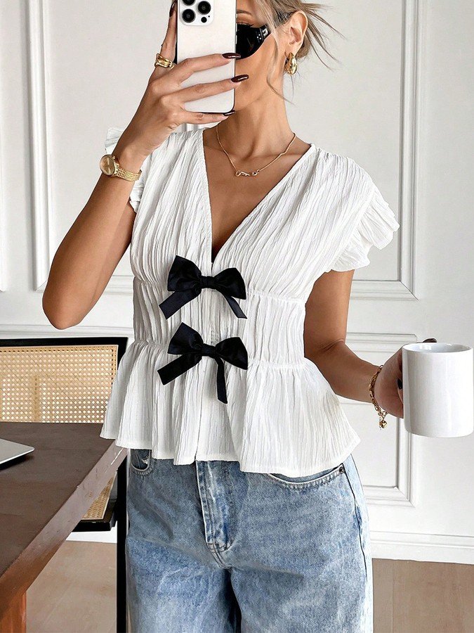 Front view of the white and black bow-front flutter-sleeve blouse, showing its silhouette and design details.