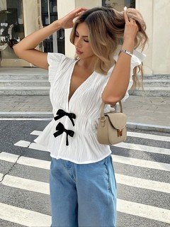 Angled front view of the white and black bow-front flutter-sleeve blouse, showing its silhouette and design details.