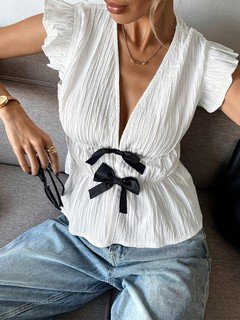 Close-up of the white and black bow-front flutter-sleeve blouse, showing its silhouette and design details.