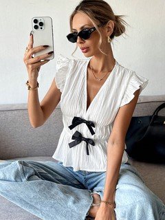 Full-length front view of the white and black bow-front flutter-sleeve blouse, showing its silhouette and design details.