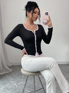 Seated front view of the black contrast-piping tie-front long-sleeve top, showing the silhouette and fit.