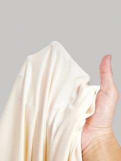 Stretch detail of the ivory draped ruched asymmetric flared-sleeve top, showing asymmetric hem, side ruching and flared cuffs.