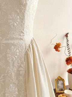 Fabric detail of the ivory floral-embossed square-neck sleeveless midi dress, showing raised floral texture, square neckline and midi skirt.