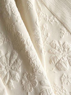 Floral texture detail of the ivory floral-embossed square-neck sleeveless midi dress, showing raised floral texture, square neckline and midi skirt.