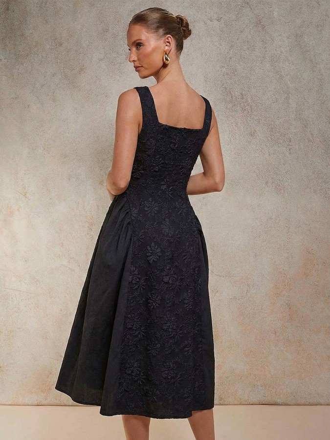 Back view of the black floral textured square-neck dress, showing its silhouette and design details.