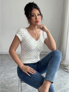 Seated front view of the white polka-dot lace-trim v-neck short-sleeve top, showing the silhouette and fit.