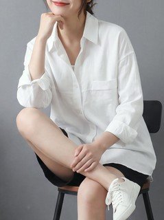 Seated front view of the white relaxed button-up long-sleeve shirt, showing the silhouette and fit.