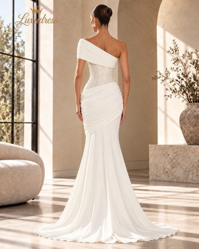 Back view of an ivory beaded mermaid gown showing a lace-up corset back, asymmetric shoulder draping and a flowing train.