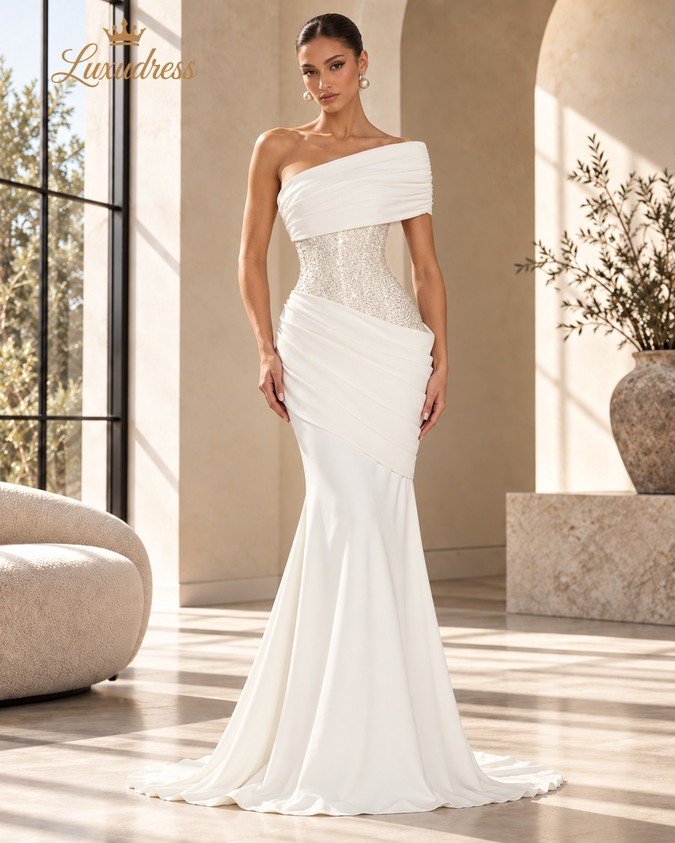 Front view of an ivory one shoulder mermaid gown with a beaded corset bodice, asymmetric draping and a fitted silhouette.