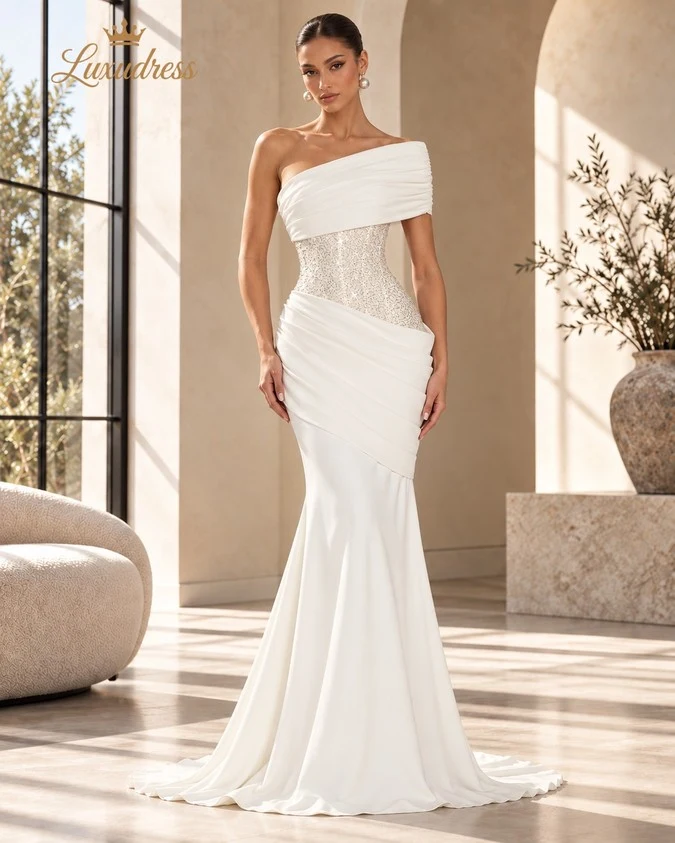Front view of an ivory one shoulder mermaid gown with a beaded corset bodice, asymmetric draping and a fitted silhouette.