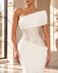 Close-up of an ivory mermaid gown showing the embellished corset bodice, one shoulder draping and diagonal hip folds.