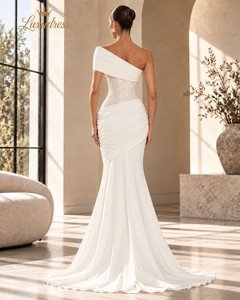Back view of an ivory beaded mermaid gown showing a lace-up corset back, asymmetric shoulder draping and a flowing train.