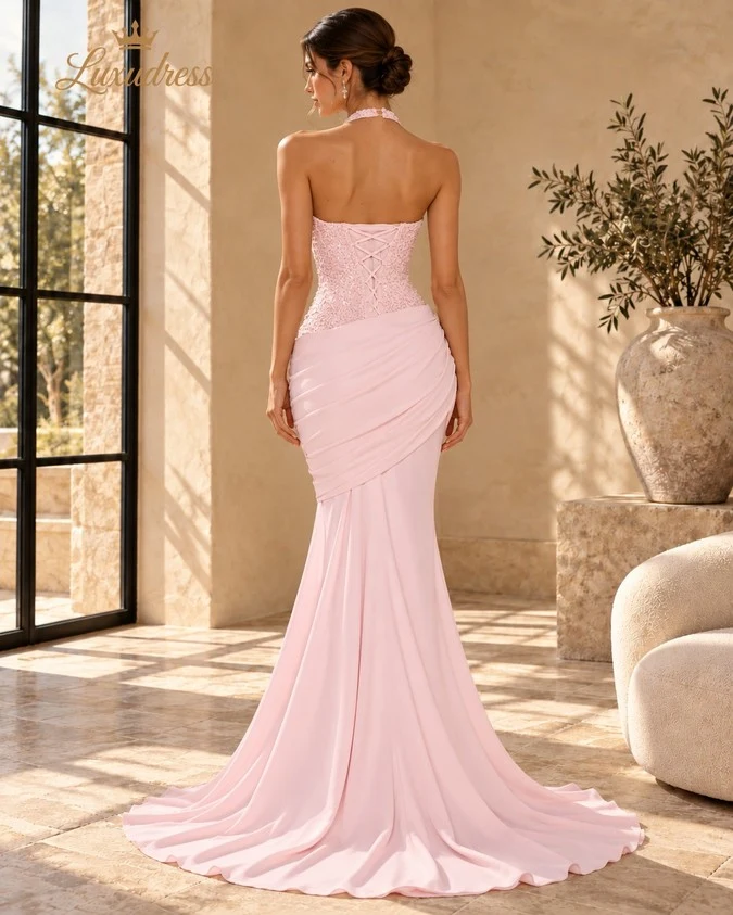 Back view of a blush pink beaded mermaid prom dress showing a lace-up bodice, draped hips and a flowing train.