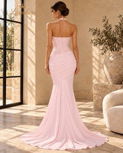 Back view of a blush pink beaded mermaid prom dress showing a lace-up bodice, draped hips and a flowing train.