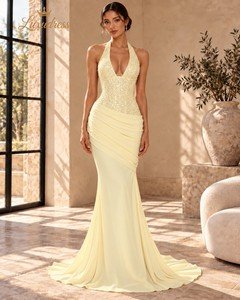Front view of a butter yellow beaded mermaid prom dress with a deep halter neckline, draped hips and a flowing train.