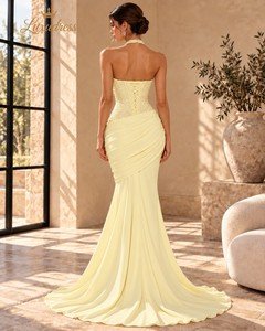 Back view of a butter yellow beaded mermaid prom dress showing a lace-up bodice, draped hips and a flowing train.