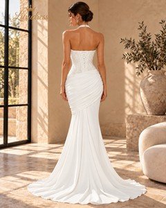 Back view of an ivory beaded mermaid prom dress showing a lace-up bodice, asymmetric hip draping and a flowing train.