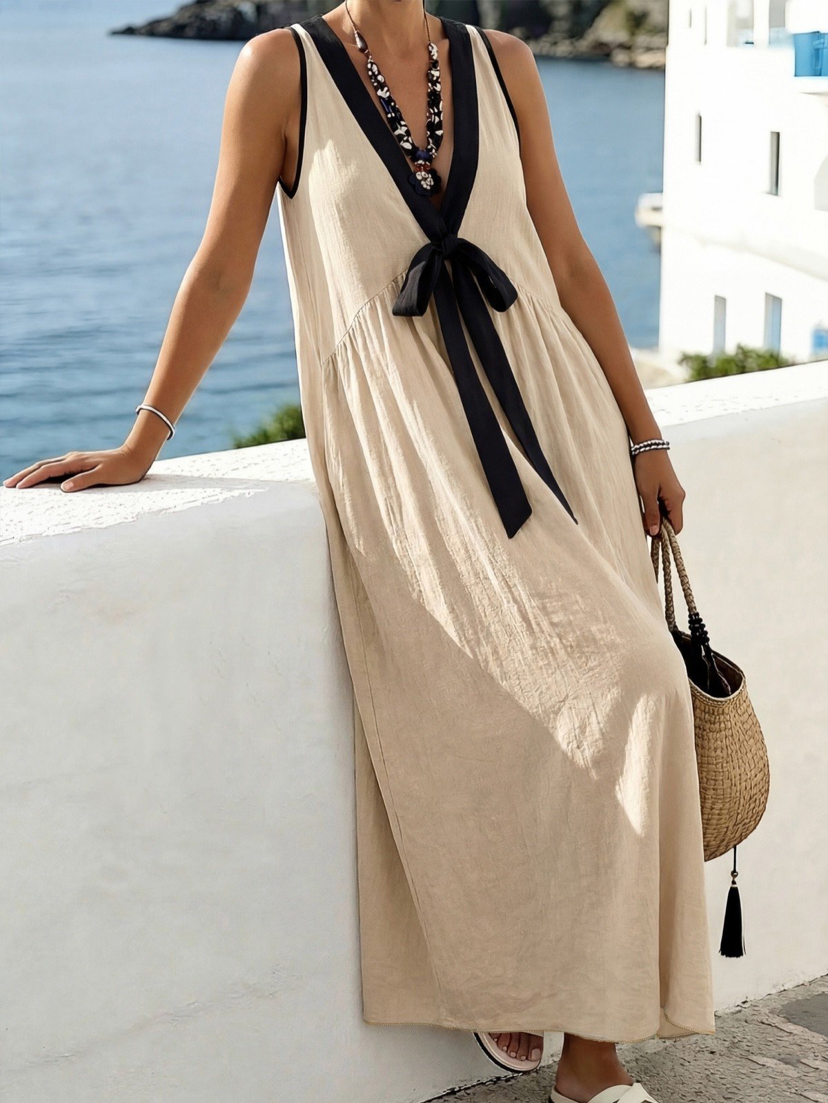 Balcony front view of a beige cotton maxi dress with black trim and a front bow tie.