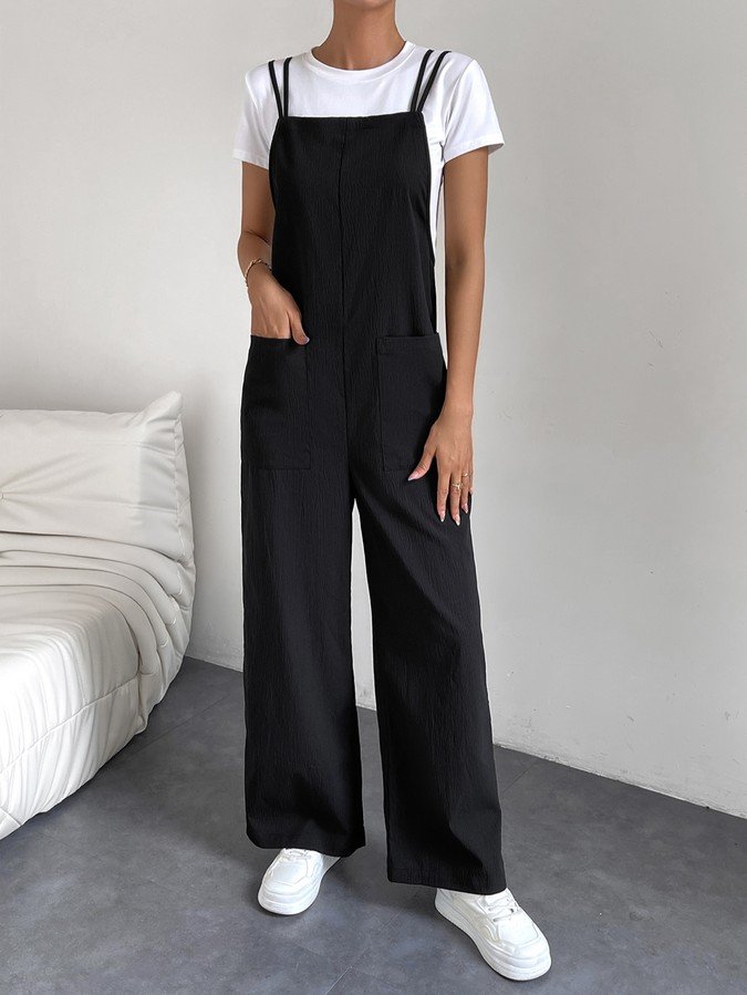 Pocket front view of a black cotton wide-leg bib overall jumpsuit with patch pockets.