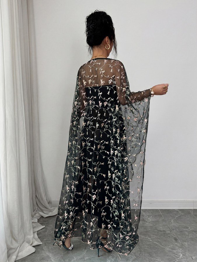 Cape back view of a black floral embroidered mesh cape maxi dress over a fitted slip.