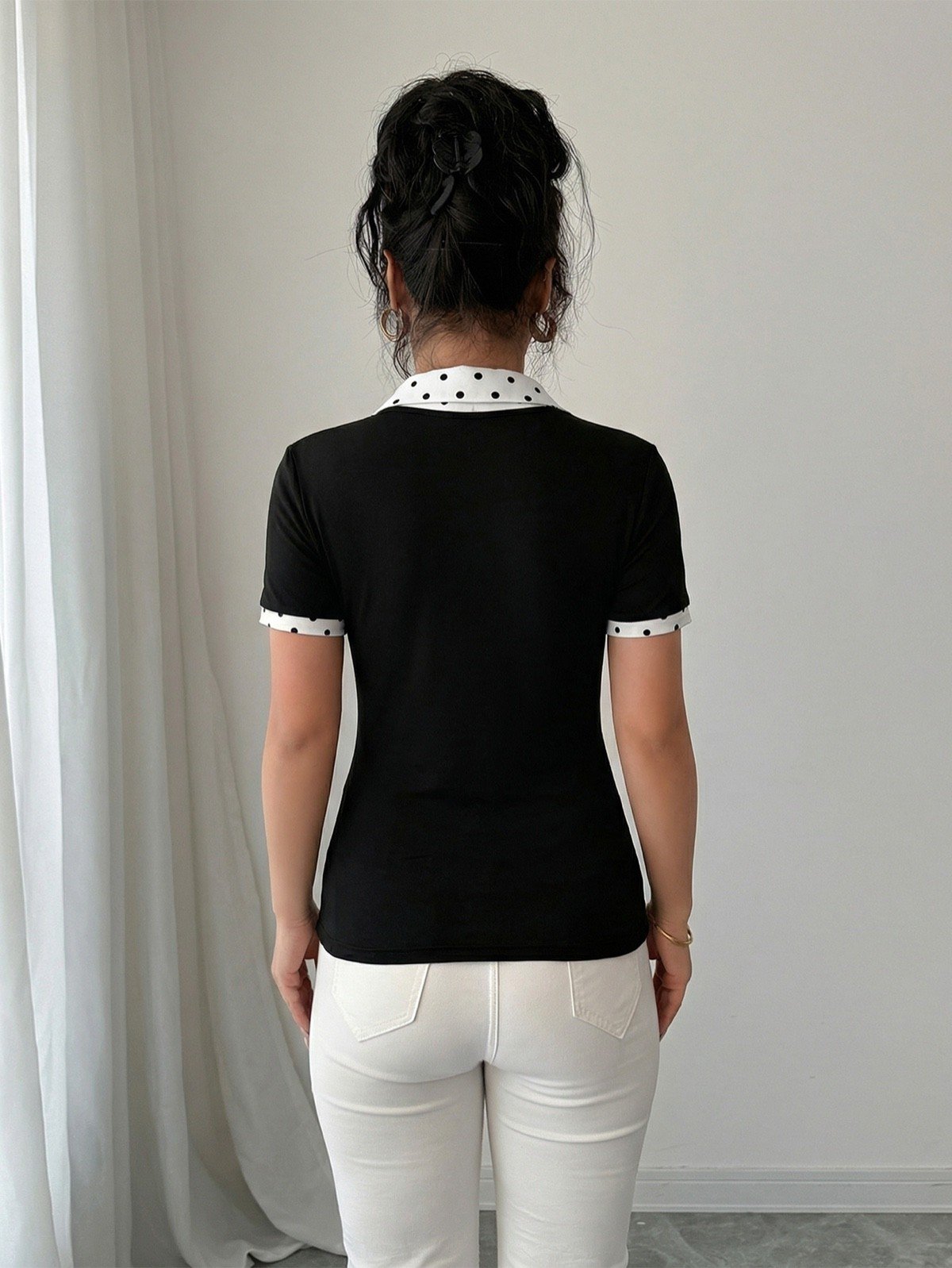 Back view of a black fitted polo top with a white polka-dot collar and cuffs.