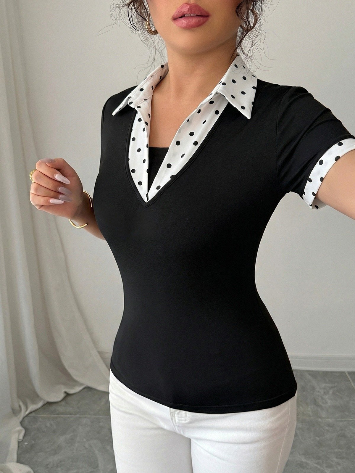 Contrast collar close-up of a black fitted polo top with a white polka-dot collar and cuffs.