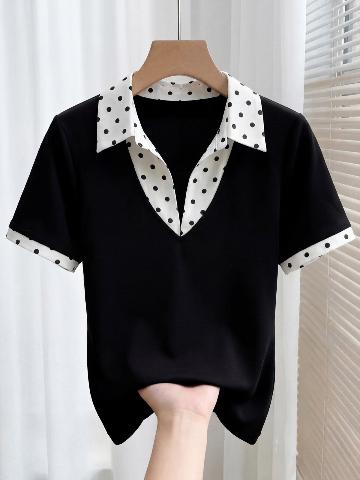 Hanger product display of a black fitted polo top with a white polka-dot collar and cuffs.