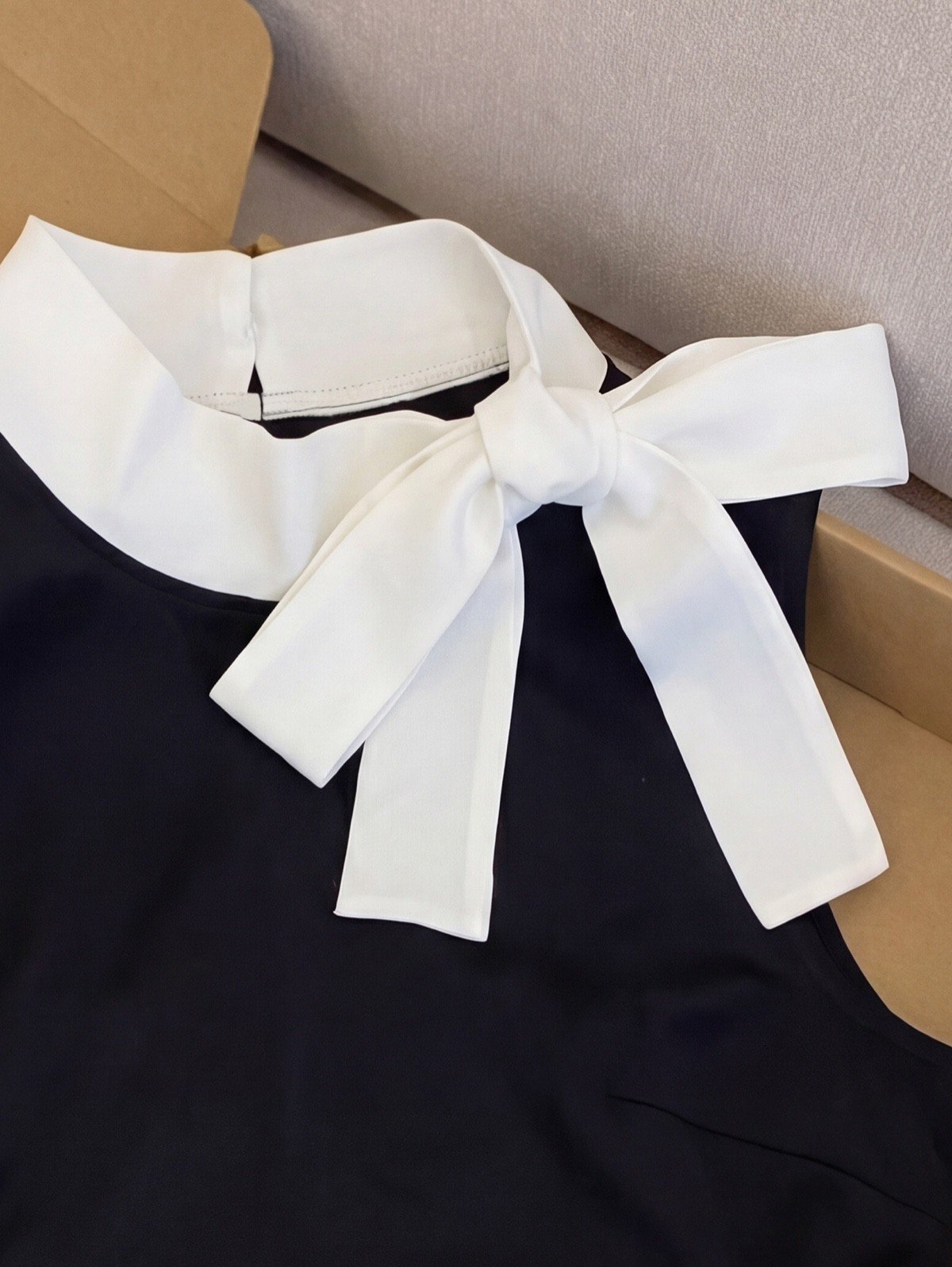 Bow collar detail of a black bow-collar blouse and white polka-dot mini skirt set.