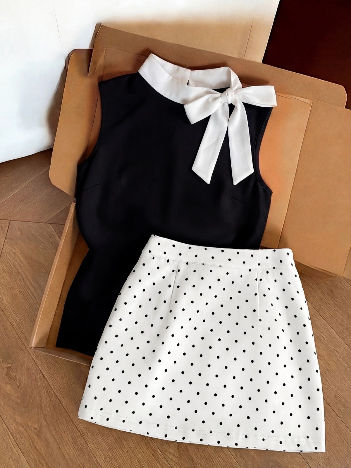 Bow Blouse and Polka-Dot Skirt Set – Primary Set Flat-Lay Primary set flat-lay of a black bow-collar blouse and white polka-dot mini skirt set.