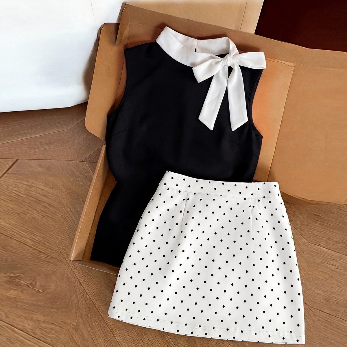 Square set flat-lay of a black bow-collar blouse and white polka-dot mini skirt set.