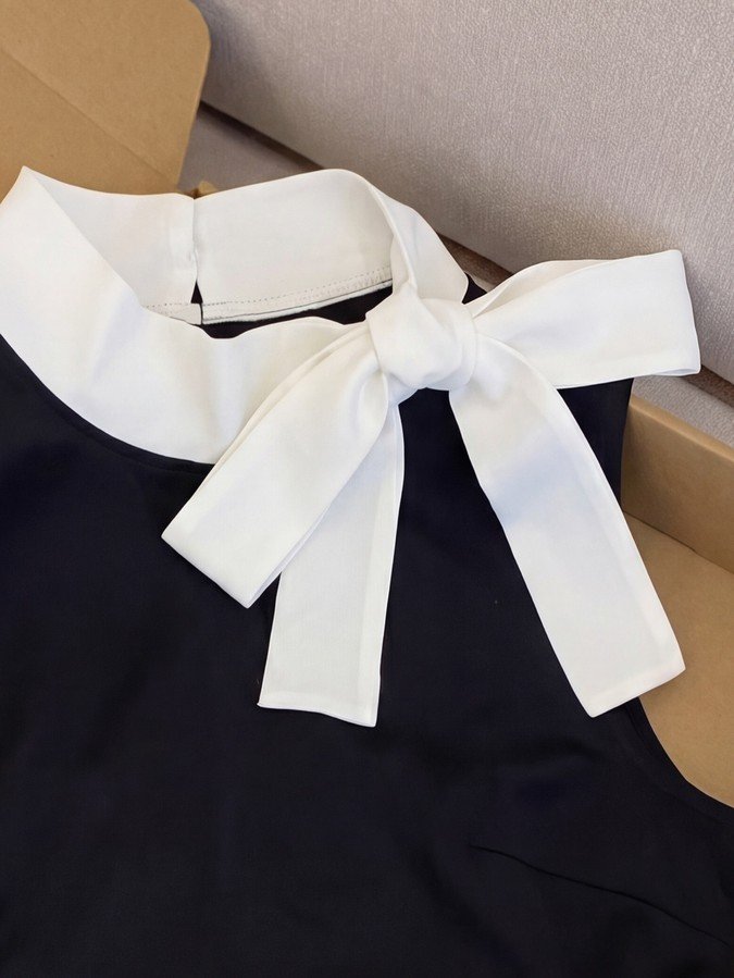 Bow collar detail of a black bow-collar blouse and white polka-dot mini skirt set.