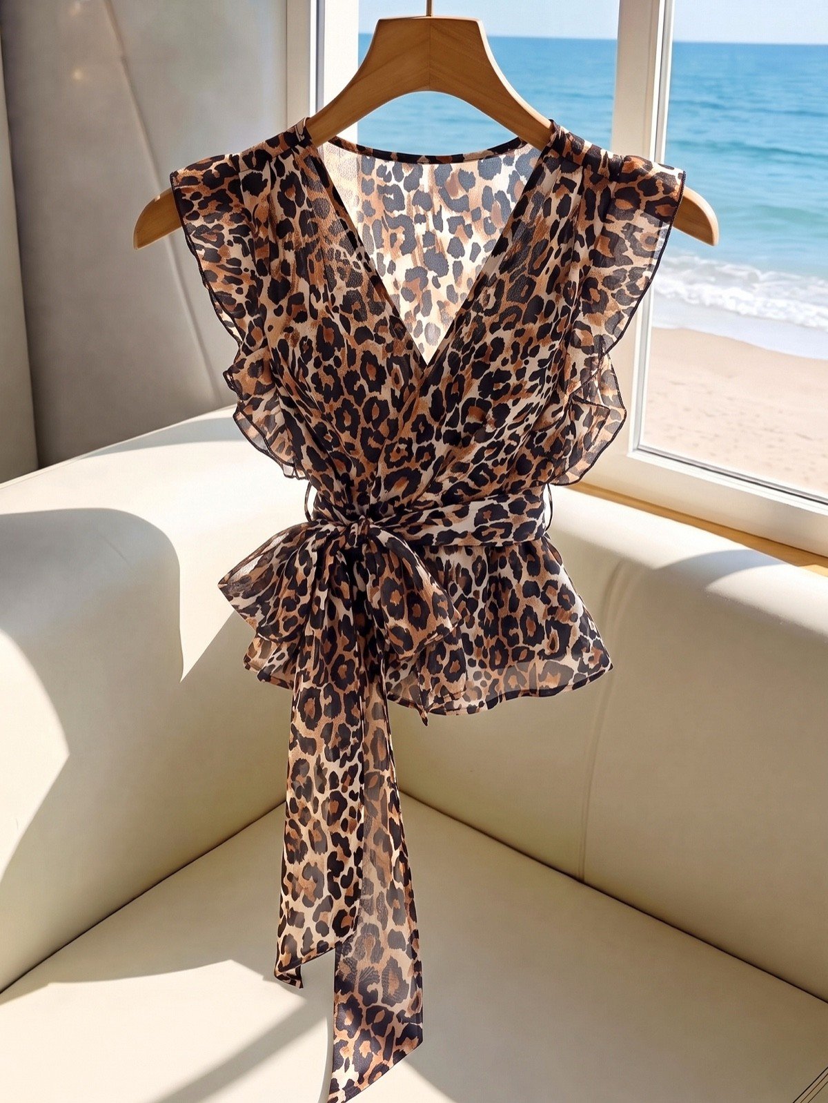 Hanger product display of a brown leopard chiffon wrap blouse with flutter sleeves and a peplum hem.