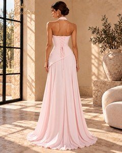 Back view of a blush pink evening gown showing a lace-up corset back, asymmetric waist overlay and floor-length skirt.