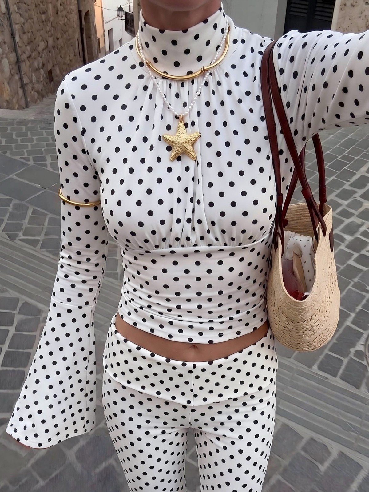 High neckline close-up of a white polka-dot bell-sleeve crop top and matching pants set.