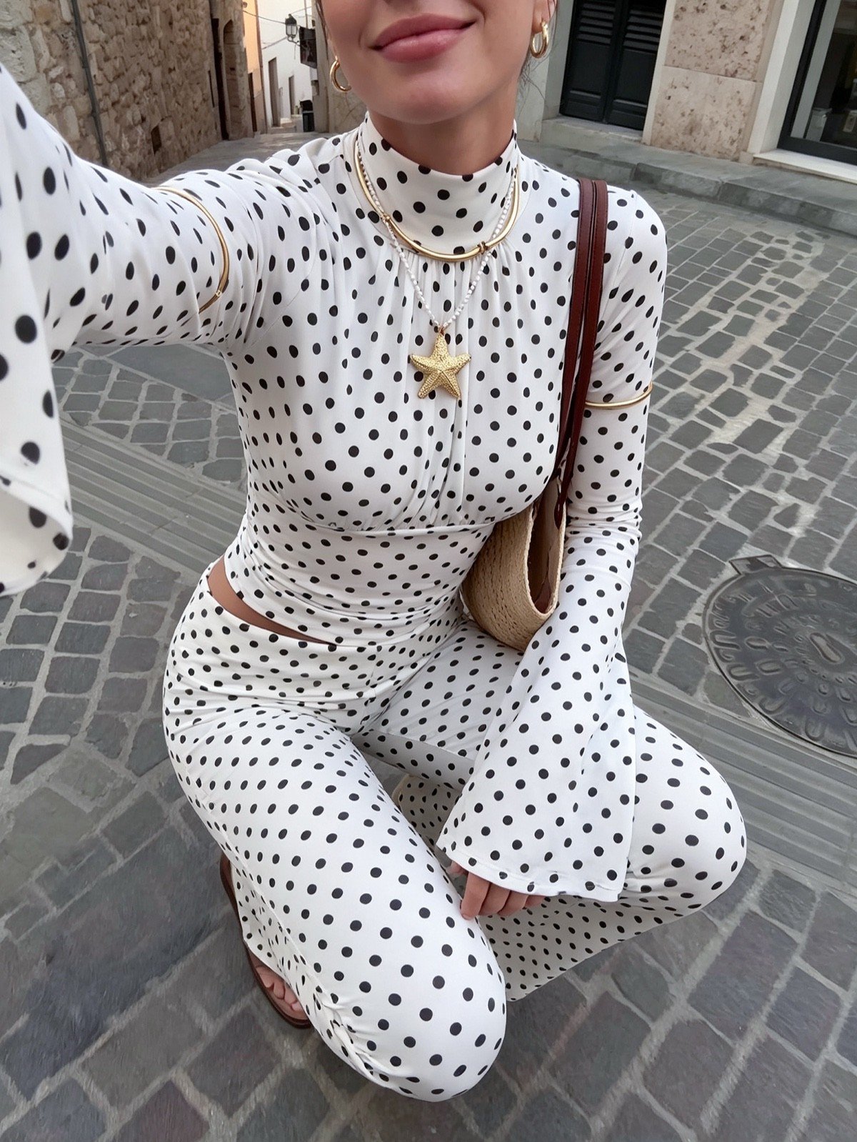 Seated front view of a white polka-dot bell-sleeve crop top and matching pants set.