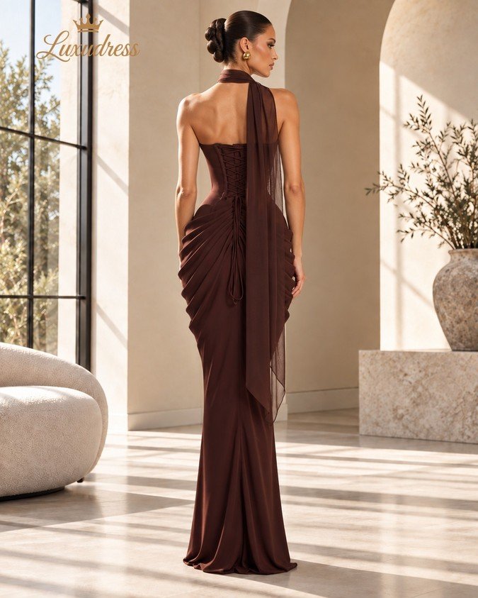 Back view of a chocolate brown corset evening gown showing lace-up fastening, ruched skirt draping and a sheer neck scarf.