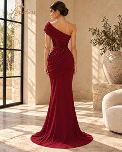 Back view of a burgundy sequin evening gown showing corset lacing, asymmetric shoulder draping and gathered folds over the hips.