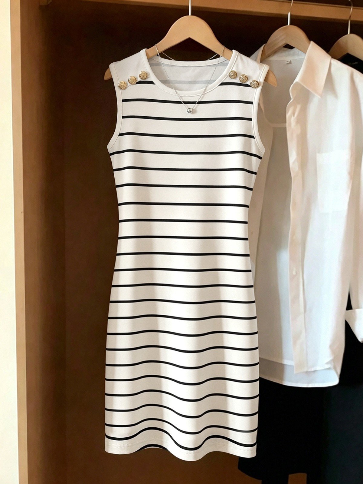 Wardrobe hanger display of a white striped knit bodycon mini dress with gold-tone shoulder buttons.