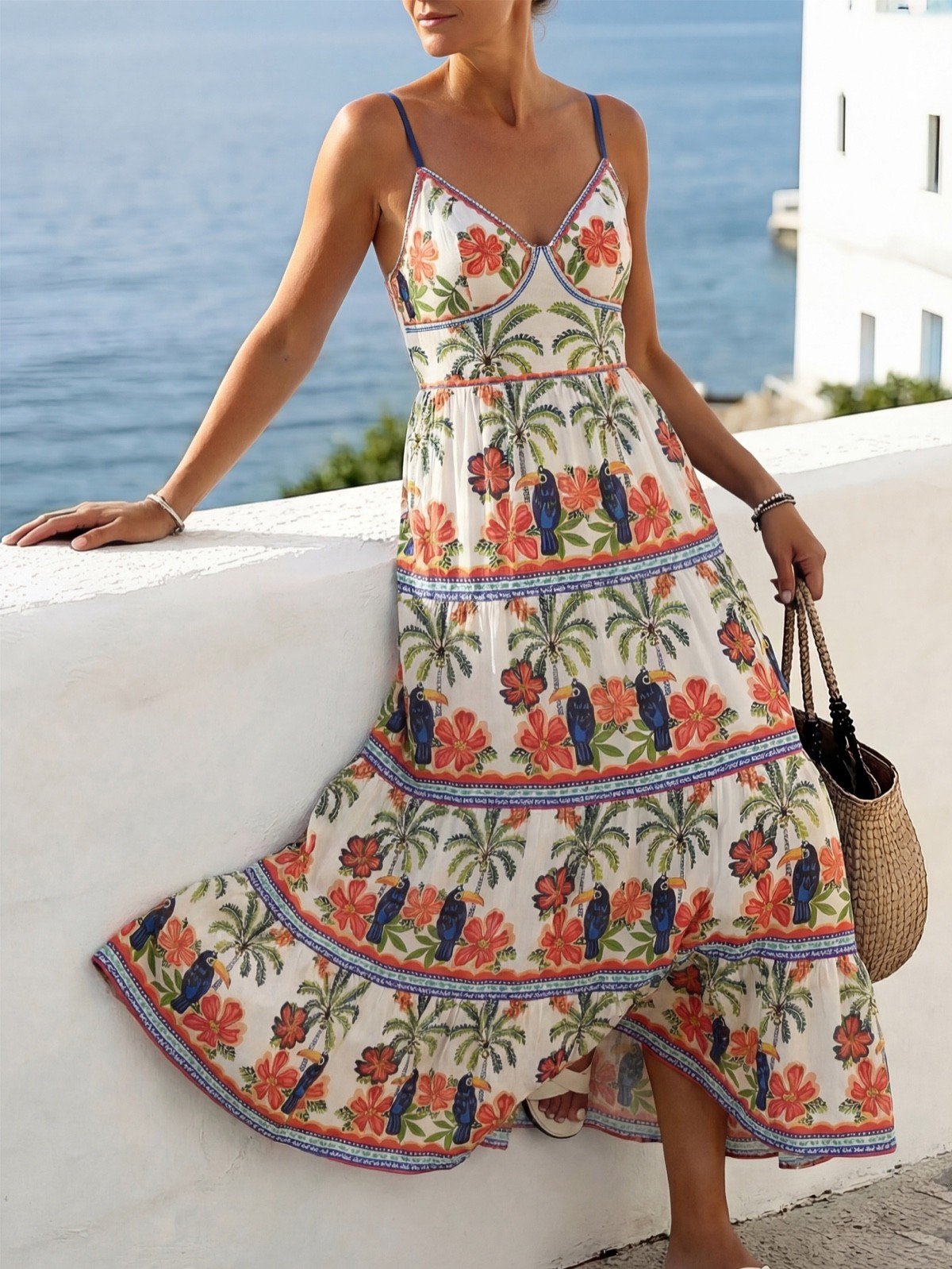 Balcony lifestyle view of a tropical print tiered maxi sundress with slim straps and a tie back.